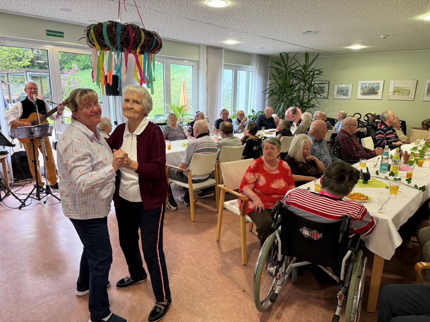 tanzende Seniorinnen und im Hintergrund die restlichen Bewohner*innen am Kaffeetisch