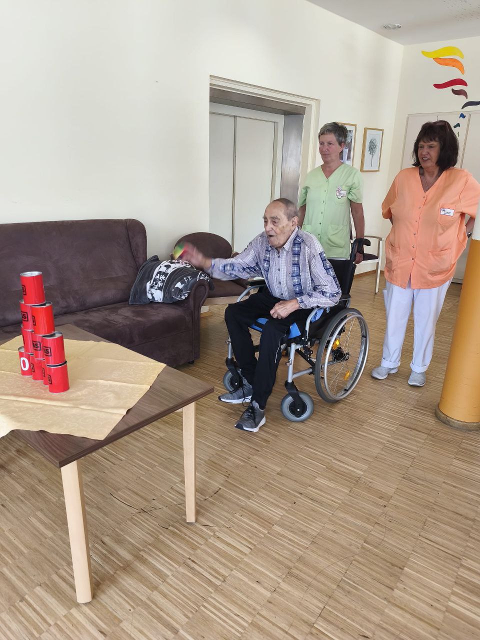 Ein Bewohner spielt ein Wurfspiel, daneben stehen zwei Pflegerinnen